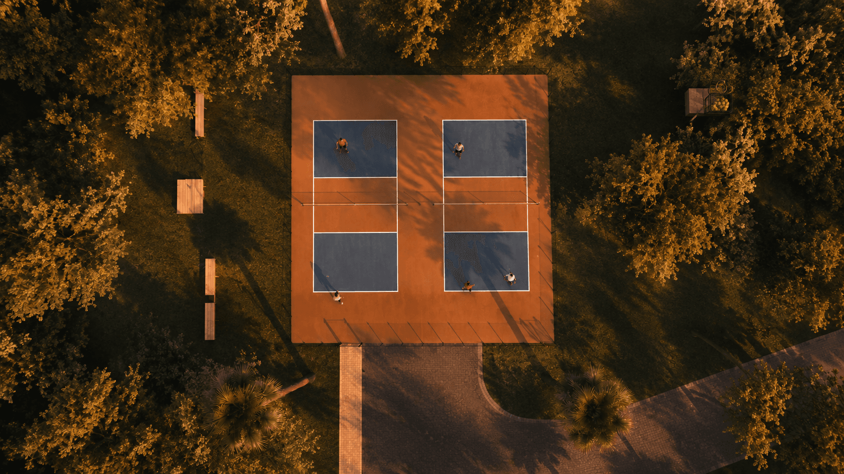 Aerial view of two clay-toned pickleball courts surrounded by trees